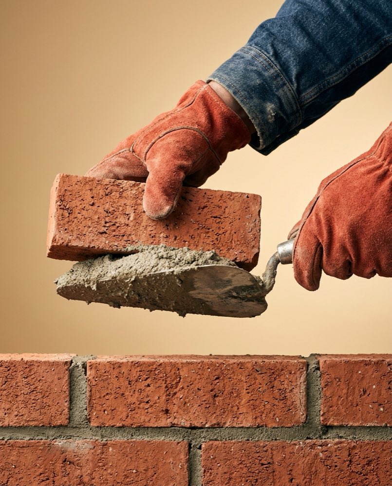 Gloved hands levelling a brick on a wet mortar course